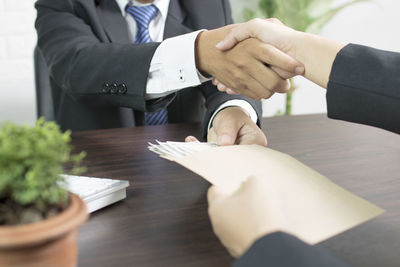 Midsection of businessman shaking hands while accepting bribe 
