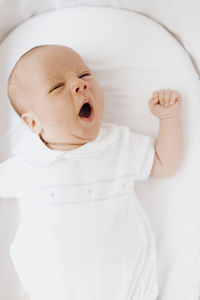 Close up newborn baby boy yawning in the crib open mouth. vertical photo.