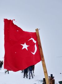 Red flag on snow covered land against clear sky