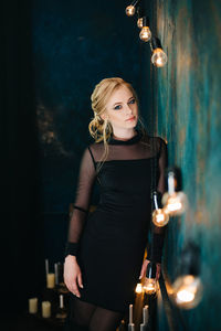 Young woman standing against illuminated wall at night