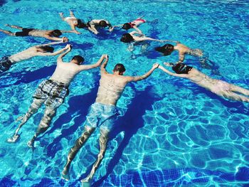High angle view of people holding hands in swimming pool during sunny day