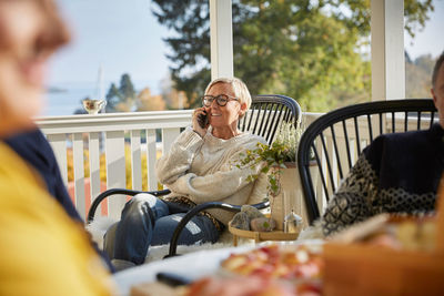 Smiling mature woman answering smart phone while sitting on porch