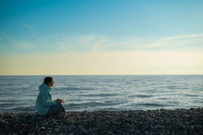 Side view of woman using laptop at seashore