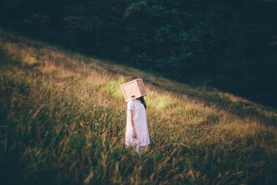 High angle view of woman hiding face with wooden box while standing on field