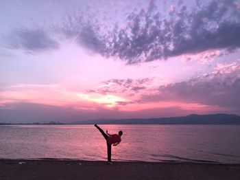 Silhouette woman exercising at beach against sky during sunset