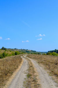 Dirt road amidst field against blue sky