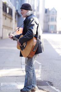 Side view of man playing guitar on street