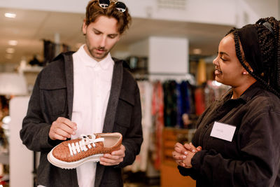 Smiling saleswoman showing shoe to male customer at retail store