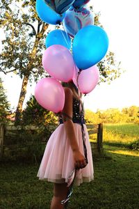 Rear view of woman with balloons standing on field