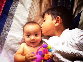 High angle view of brother kissing cute sister while lying on bed at home