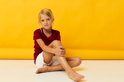 Portrait of young woman sitting against yellow background