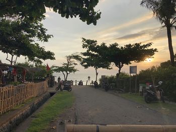 People on footpath by street against sky during sunset