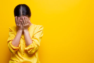 Woman covering face against yellow background