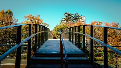 Footbridge amidst trees against clear blue sky