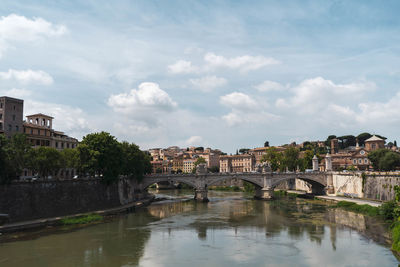 Arch bridge over river by buildings against sky