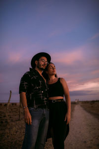 Young couple standing against sky during sunset