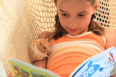 Cute girl with hamster reading book in hammock