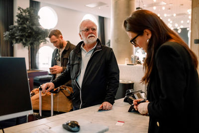 Senior man looking away while standing with receptionist at reception in hotel