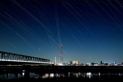 Low angle view of star trails over bridge at night