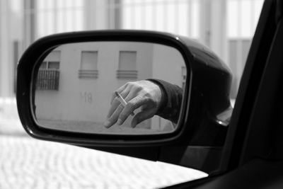 Cropped image of hand holding cigarette seen in side-view mirror