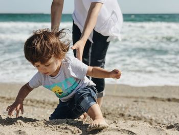 Low section of woman holding boy playing on sand at beach