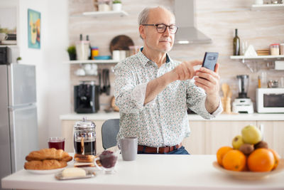 Senior man using mobile phone at kitchen