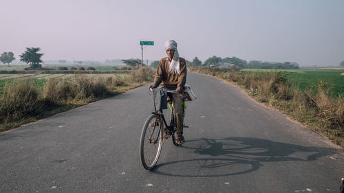 Man riding bicycle on road against sky