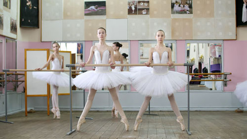 In the ballet hall, girls in white ballet tutus, packs are engaged at ballet, rehearse plie forward