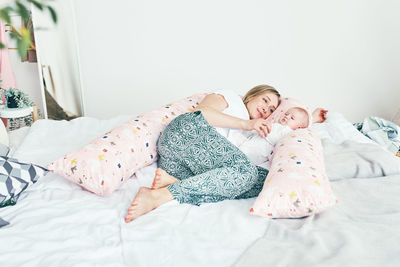 Full length of mother lying down on bed with daughter
