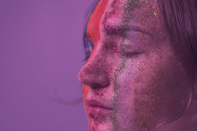 Close-up woman with painted face and closed eyes against purple background