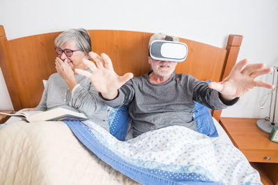 Senior man using virtual reality by woman on bed