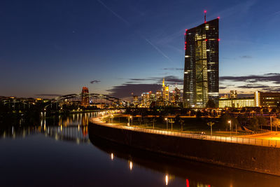 Illuminated buildings by river against sky at night