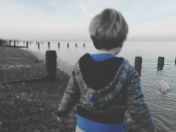 Rear view of boy standing in sea against sky