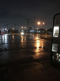 Wet road by illuminated city against sky at night