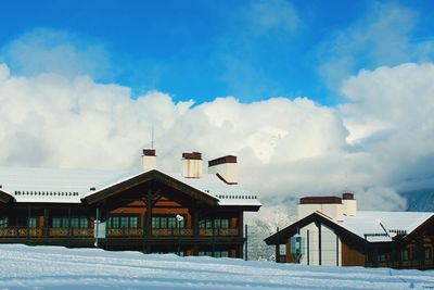 Houses on snow covered field by building against sky