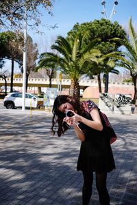 Side view of woman with sunglasses standing against trees in city