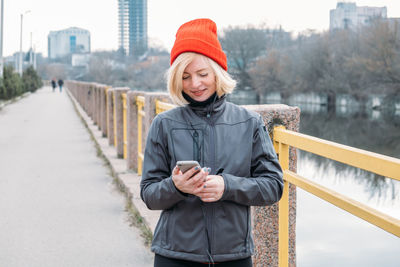 Portrait of smiling woman standing on railing in city during winter