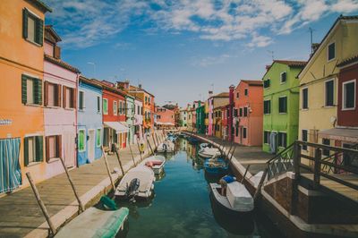 Boats moored in canal amidst buildings in city against sky