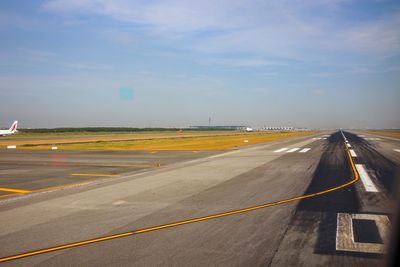 Road by airport runway against sky