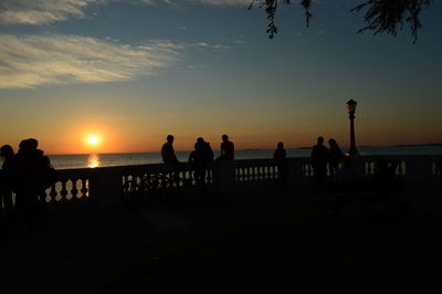 Silhouette people standing on beach against sky during sunset