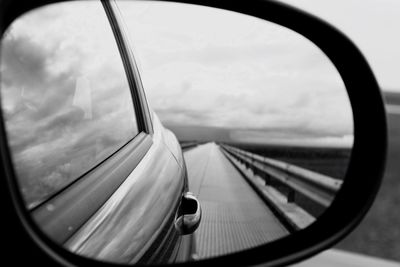 Reflection of road against cloudy sky in side-view mirror of car