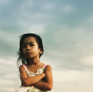 Girl with arms crossed looking away against sky