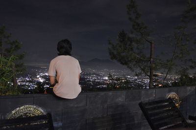 Rear view of man looking at illuminated city against sky