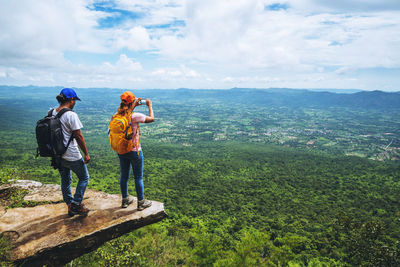 Rear view of man and woman standing on cliff against sky