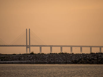 Bridge over sea against orange sky
