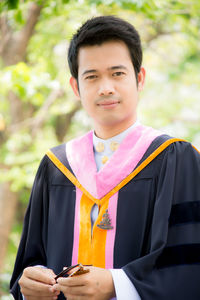 Portrait of mid adult man wearing graduation gown while standing outdoors