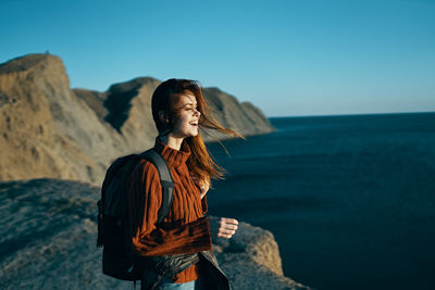 Young woman looking away while standing on rock in sea against sky
