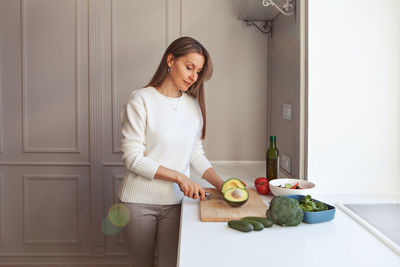 Woman cooking vegetarian salad with fresh vegetables. model cutting with knife avocados, broccoli