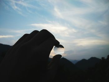 Close-up of hand holding silhouette mountain against sky