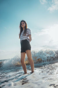 Portrait of young woman standing in sea against sky